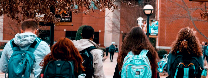 Back view of students with backpacks walking towards a learning center, a typical scene for those heading to Spanish classes in Medellín, Colombia, immersed in learning Colombia Spanish.