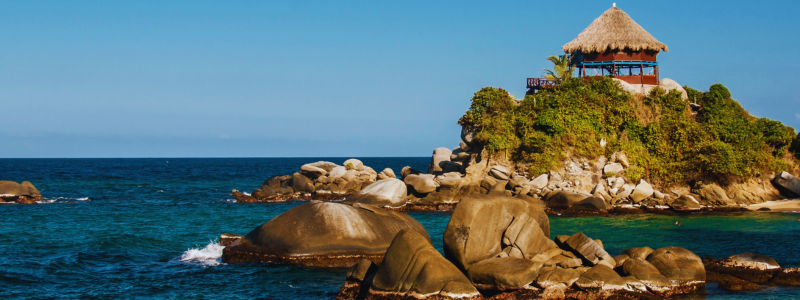 Scenic view of the unique rock formations and traditional thatched-roof hut in Parque Tayrona, a prime example of Colombian places ideal for cultural immersion and language learning for students of Colombia Spanish in Medellín.